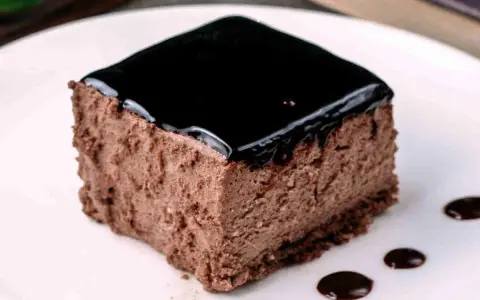 Un delizioso semifreddo al cioccolato, con una lucida glassa scura e gocce di salsa al cioccolato sul piatto bianco.
