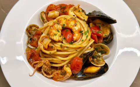 Un piatto invitante di spaghetti allo scoglio, con gamberi, cozze, vongole e calamari, condito con pomodorini freschi e prezzemolo.