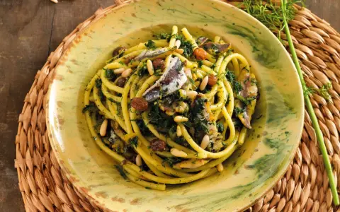 Un piatto di pasta con le sarde, condita con finocchietto selvatico, pinoli e uvetta, servita in un piatto decorato.