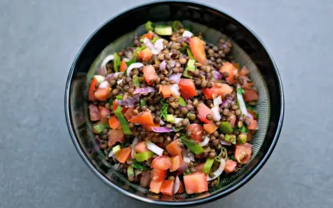 Una ciotola di insalata di lenticchie colorata con pomodori, cipolla rossa e erbe fresche.