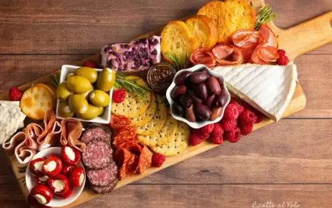 Un invitante tagliere salumi e formaggi con olive, lamponi, pane tostato e formaggio cremoso, perfetto per un aperitivo.