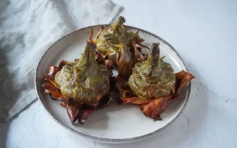Tre carciofi alla giudia dorati e croccanti su un piatto, pronti per essere gustati.
