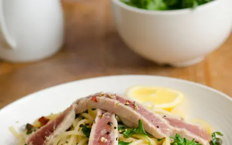 Spaghetti con tonno fresco alla siciliana, guarniti con rucola, capperi, pomodori secchi e una fetta di limone.