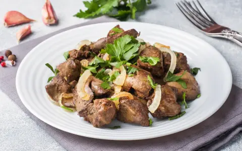 Piatto di fegato alla veneziana con cipolle e prezzemolo, contornato da aglio e pepe.