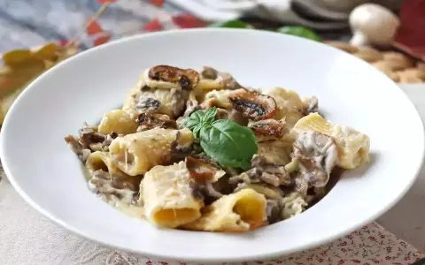 Un piatto invitante di pasta funghi e panna, con rigatoni conditi generosamente e guarniti con basilico fresco.
