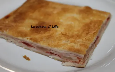 Una fetta di torta salata prosciutto e formaggio, con pasta sfoglia dorata e ripieno filante.
