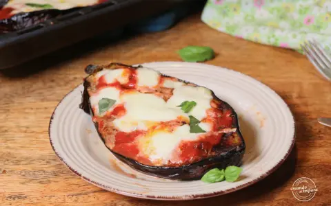 Melanzane alla pizzaiola appena sfornate, con mozzarella filante e basilico fresco su un piatto rustico.