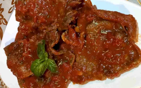 Fette di carne alla pizzaiola, ricoperte da un sugo rosso saporito e guarnite con basilico fresco.