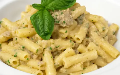 Un piatto invitante di pasta con melanzane in bianco cremosa, guarnito con basilico fresco.