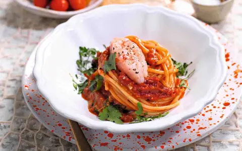 Spaghetti con gamberetti e pomodorini alla siciliana, un piatto colorato e saporito, guarnito con prezzemolo fresco.