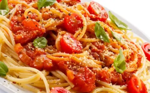 Un piatto di spaghetti alla carrettiera, conditi con pomodoro fresco, basilico e parmigiano grattugiato.