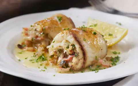 Deliziosi involtini di pesce spada ripieni, serviti su un piatto bianco con spicchio di limone e prezzemolo tritato.