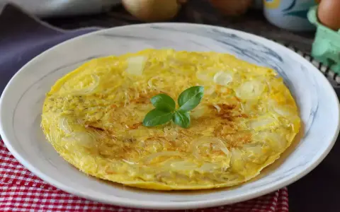 Una dorata frittata di cipolle, guarnita con basilico fresco, servita su un piatto bianco.
