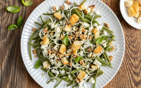 Deliziosa insalata di fagiolini con formaggio feta, noci croccanti, crostini e cipolla rossa. Un piatto fresco e saporito.