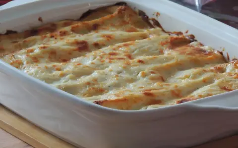Lasagne con carciofi, besciamella e mozzarella appena sfornate, dorate e filanti in una teglia bianca.