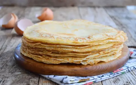 Pila di crepes dorate, perfette per una crepes ricetta senza burro. Guscio d'uovo sullo sfondo.