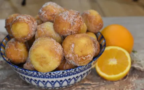 Arancini dolci, soffici arrubiolus di ricotta cosparsi di zucchero, accanto a fette d'arancia.