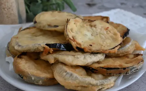 Piatto di melanzane fritte pastellate, dorate e croccanti, pronte per essere gustate.