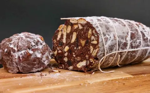 Salame al cioccolato vegano, un dolce goloso con biscotti e frutta secca, spolverato di zucchero a velo.