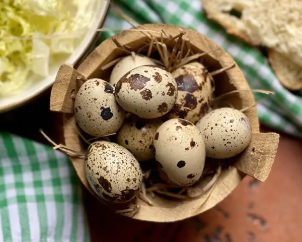 Un cesto di paglia contiene uova di quaglia sode, pronte per essere gustate. Accanto, un'insalata fresca e pane.