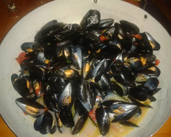 Un'abbondante impepata di cozze in un piatto largo, con pomodorini e un sughetto invitante.