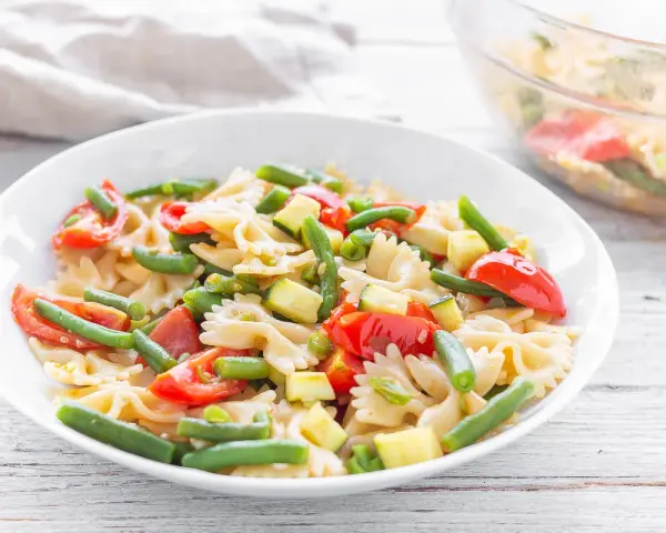 Un piatto invitante di pasta fredda vegana con farfalle, pomodorini, zucchine e fagiolini. Perfetta per un pasto leggero e gustoso.