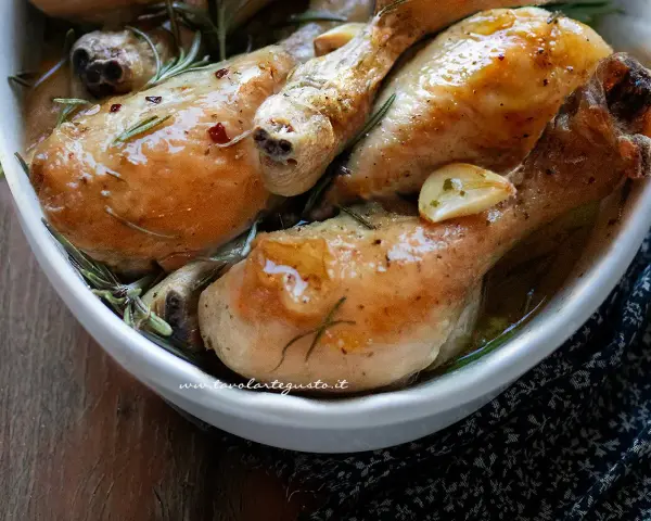 Cosce di pollo al forno succulente, dorate e profumate al rosmarino e aglio, servite in una ciotola bianca.