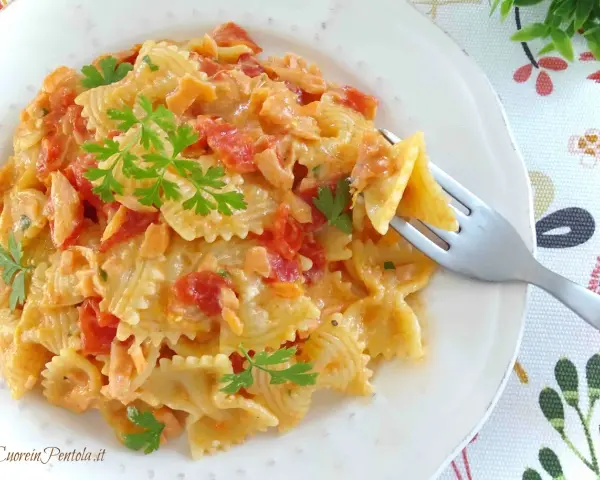 Farfalle cremose con pomodorini e salmone, guarnite con prezzemolo fresco. Un piatto invitante pronto per essere gustato.