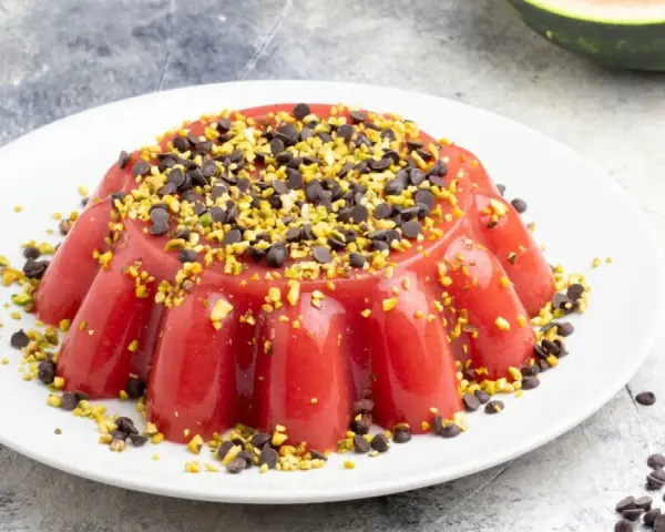 Delizioso gelo di melone rosso, guarnito con gocce di cioccolato e pistacchi tritati, su un piatto bianco.