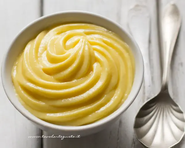 Una ciotola di soffice crema pasticcera, pronta per essere gustata. Accanto, un cucchiaio d'argento.