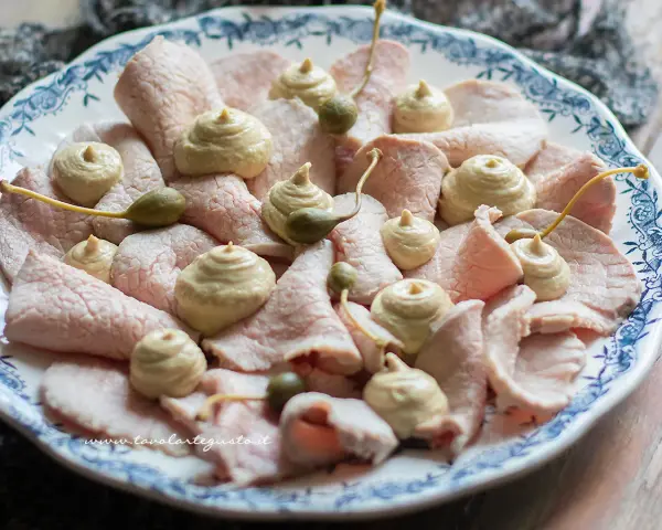 Piatto di vitello tonnato con salsa cremosa, capperi e guarnizioni.