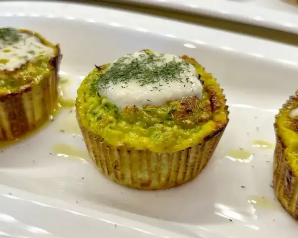 Tre tortini di zucchine dorati, guarniti con formaggio fuso e aneto, serviti su un piatto bianco.