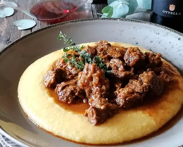 Un piatto di gulash con polenta fumante, guarnito con rametti di timo fresco. Un classico confortante, perfetto per una cena speciale.