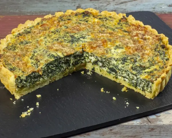 Una fetta di torta salata ricotta e spinaci, con crosta dorata e ripieno cremoso, su una lavagna scura.