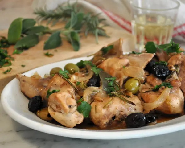 Piatto di coniglio alla cacciatora in bianco, con olive verdi e nere, cipolle e rosmarino.