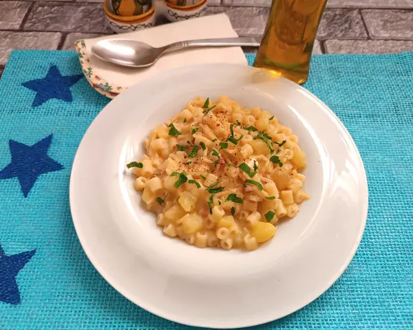 Un piatto di pasta patate e provola fumante, guarnito con prezzemolo fresco e un pizzico di peperoncino, pronto per essere gustato.