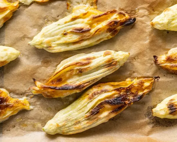 Fiori di zucca in pastella dorati e croccanti, appena sfornati su carta da forno.