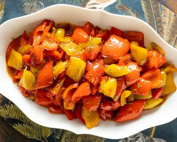 Peperoni in umido, colorati e succulenti, conditi con erbe aromatiche, serviti in una ciotola bianca su un tovagliolo decorato.