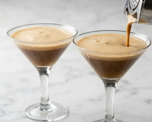 Due bicchieri di **caffè shakerato** con una schiuma densa e invitante. Uno viene riempito da uno shaker.