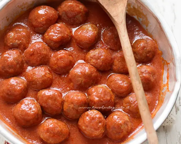 Succulente polpette di carne in un sugo rosso, pronte per essere gustate. Un cucchiaio di legno attende di servirle.