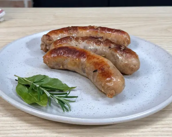 Tre salsicce dorate in padella, servite su un piatto con rosmarino e alloro.
