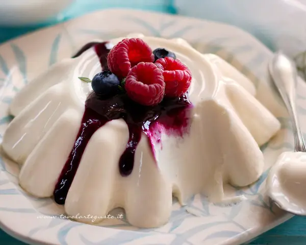 Deliziosa panna cotta con frutti di bosco e salsa ai mirtilli, servita su un piatto decorato.