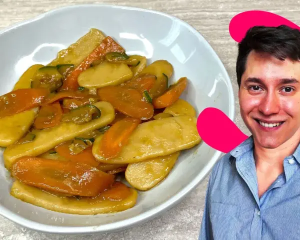 Un uomo sorride accanto a un piatto di gnocchi di riso con carote e zucchine.