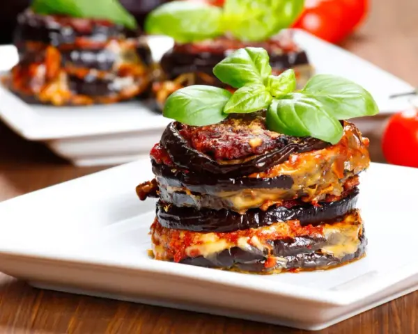 Parmigiana di melanzane, un classico della cucina italiana, servita su un piatto bianco con basilico fresco.