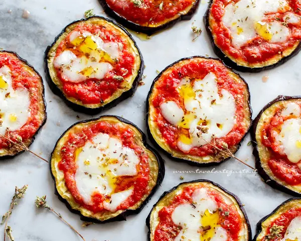 Pizzette di melanzane al forno, con pomodoro, mozzarella filante e un filo d'olio. Un antipasto sfizioso e leggero.