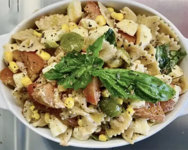Un'insalata di pasta colorata con farfalle, pomodori, mais, olive verdi e basilico fresco, condita con erbe aromatiche.
