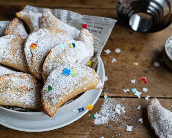 Cassatelle siciliane al forno, dolcetti dorati cosparsi di zucchero a velo e decorati con coriandoli colorati, pronti per essere gustati.