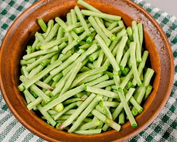 Fagiolini freschi, tagliati e pronti per essere cucinati in umido, in una ciotola di terracotta su una tovaglia a quadri verdi.