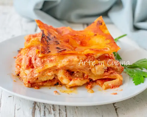 Una fetta di lasagna di mare napoletana, ricca e saporita, servita su un piatto bianco con un rametto di prezzemolo.