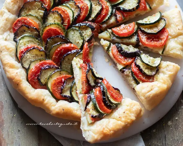 Una deliziosa torta salata estiva con zucchine, melanzane e pomodori disposti a raggiera su una base croccante.